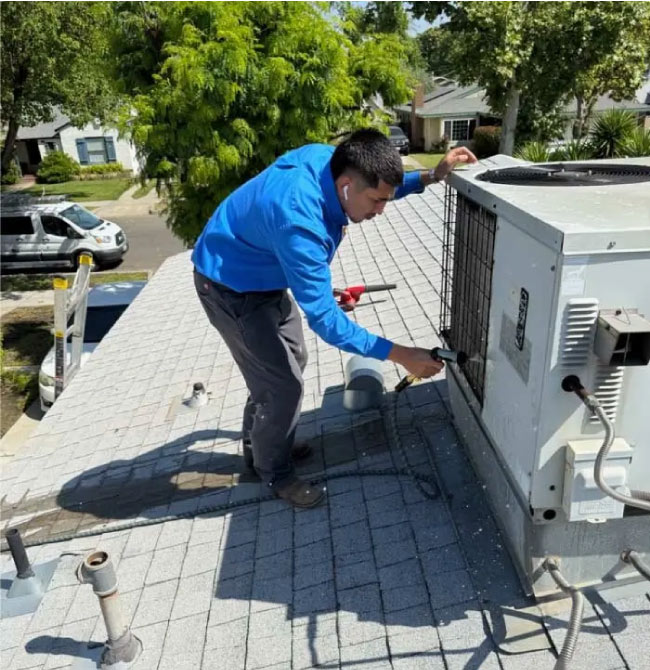 A technician is using a hose to clean/flush the coils of a rooftop AC unit.