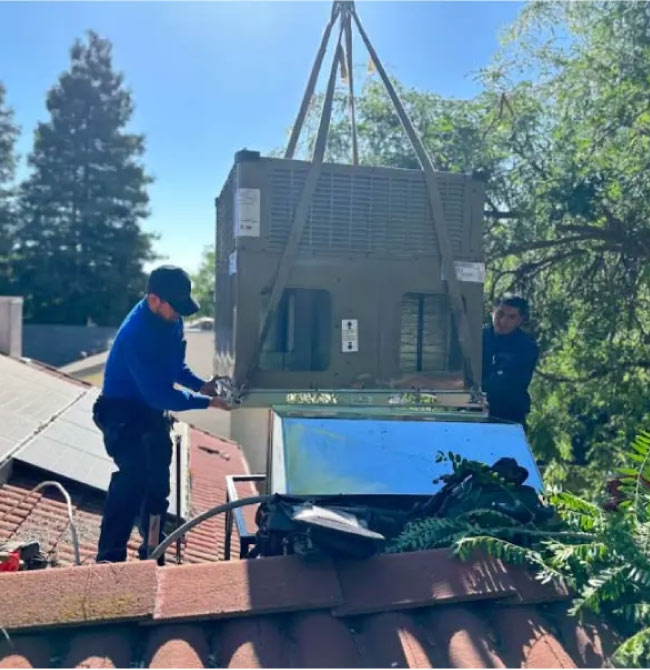 A crane is lowering a unit onto a residential roof while technicians guide it into place.