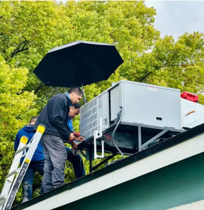 Technicians working under a black umbrella for shade/protection while servicing a unit.