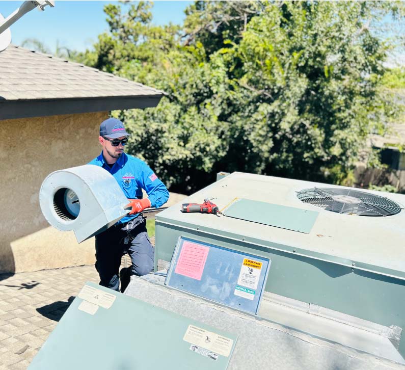Mechanical Air technician removing a blower motor assembly from a rooftop AC package unit to fix airflow issues during a repair service in Fresno CA