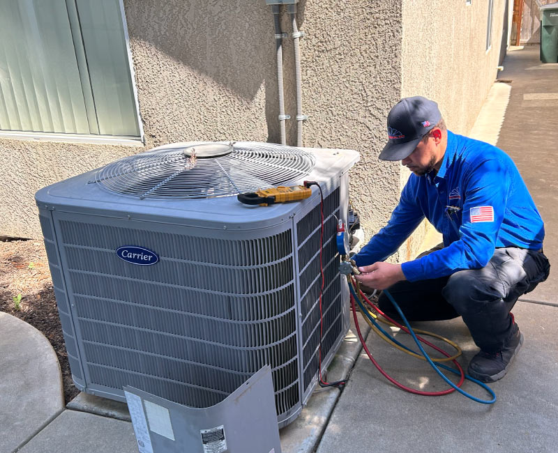 Mechanical Air technician performing diagnostics on a residential Carrier outdoor AC unit using manifold gauges and a multimeter during a service call.