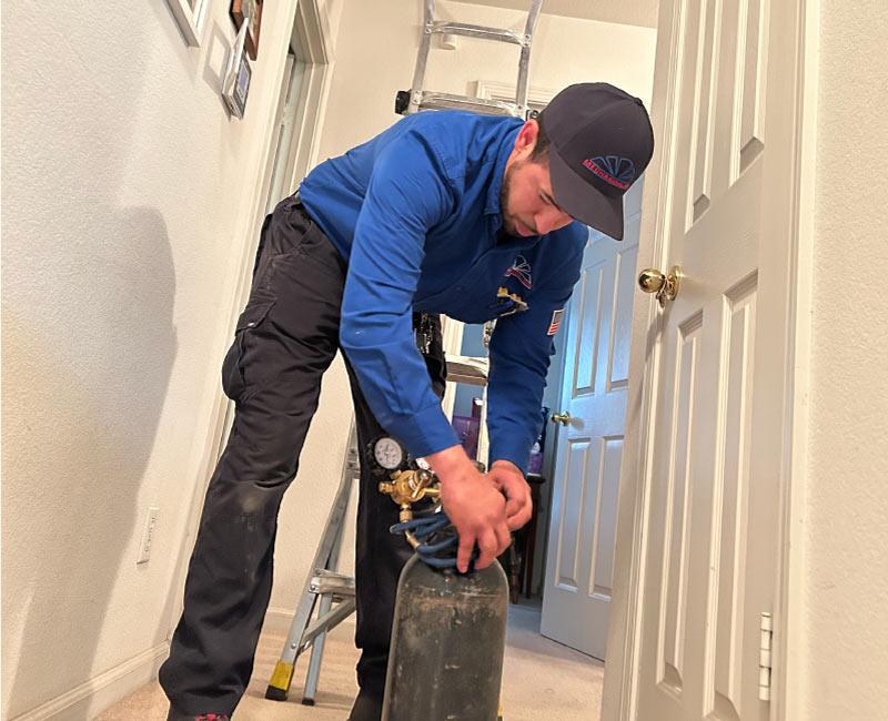Mechanical Air HVAC professional preparing a compressed gas tank and gauges for an indoor system pressure test or refrigerant charge inside a home.