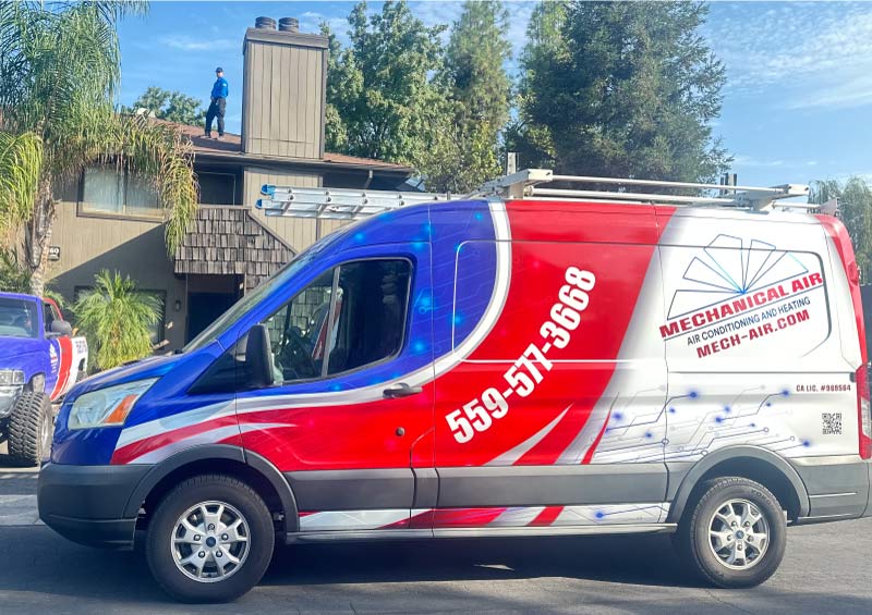 Mechanical Air service vehicle parked at a job site with a technician performing a rooftop HVAC inspection in Fresno