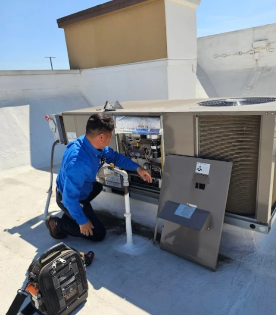 Technician inspecting the internal electrical panel of a large commercial rooftop AC package unit during a maintenance visit