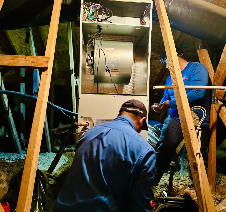 Two skilled Mechanical Air technicians performing a complex HVAC install and blower motor repair inside a residential attic to improve home energy efficiency.