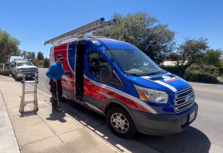 A professional Mechanical Air technician in a blue uniform prepares equipment next to a branded service van during a local residential HVAC maintenance call in the Fresno area.