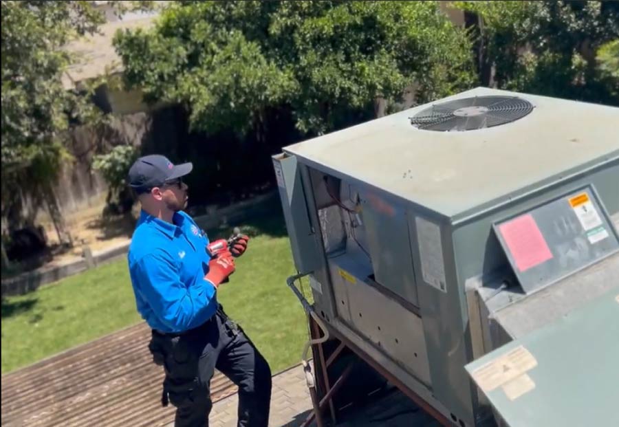 HVAC service technician using a power drill to secure the access panel during a rooftop air conditioner repair