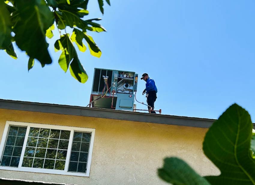 An experienced technician standing on a residential roof to diagnose an HVAC unit using pressure gauges under a clear blue sky, before an ac repair in visalia, ca