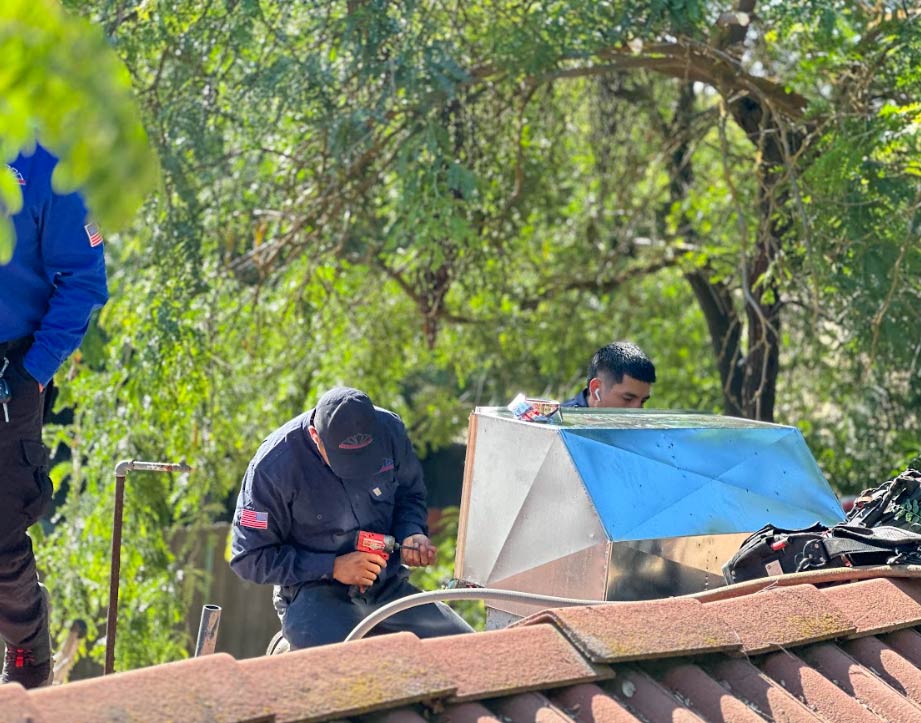 Team of HVAC professionals installing custom sheet metal ductwork and a new cooling unit on a residential tiled roof